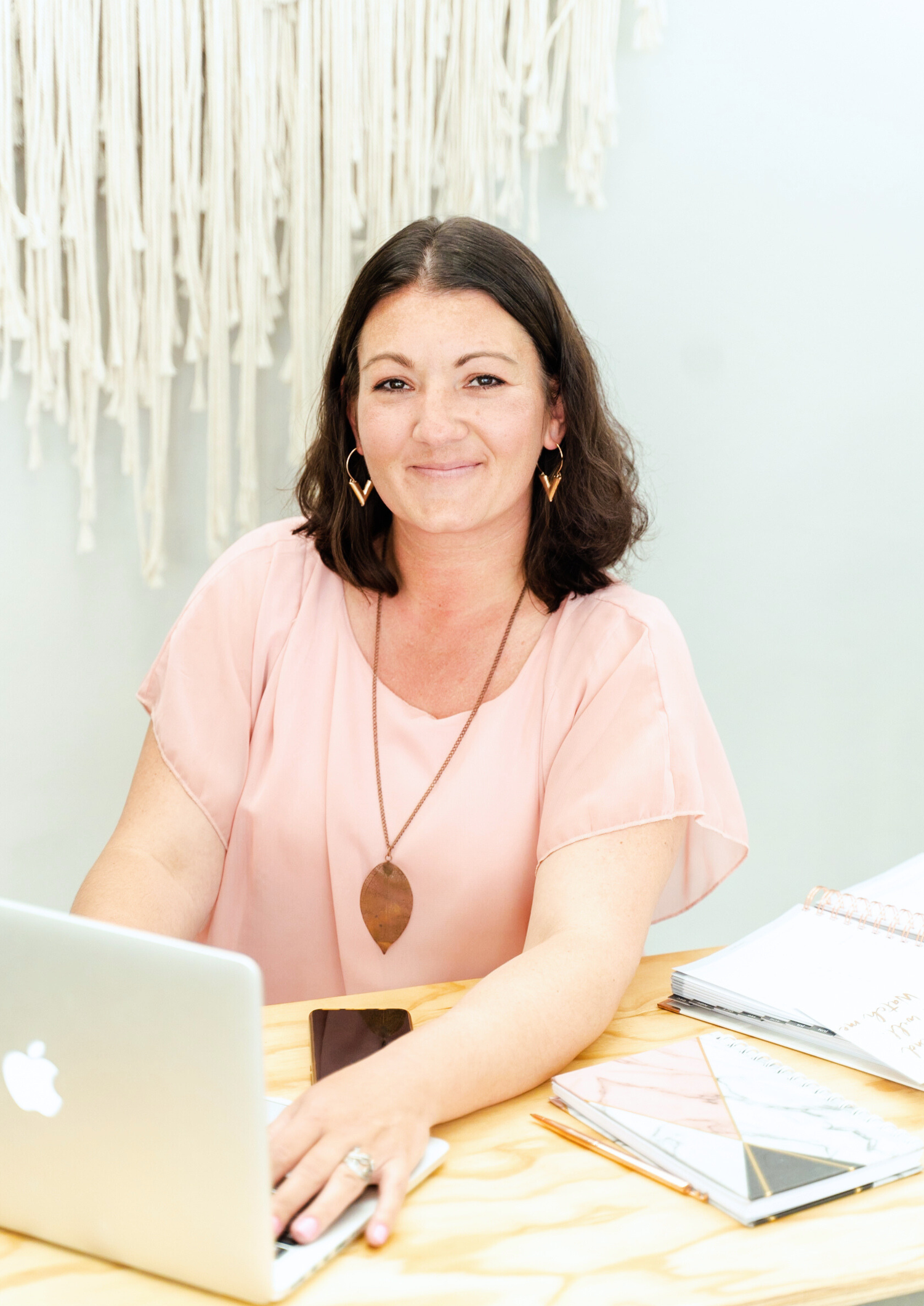 Professional wearing a pink blouse sits at desk with laptop and paperwork in modern office setting.