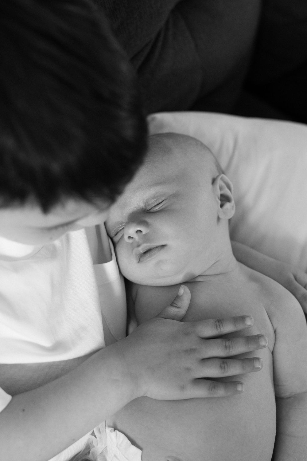 Black and white photo of parent tenderly holding and gazing at peaceful sleeping newborn baby.