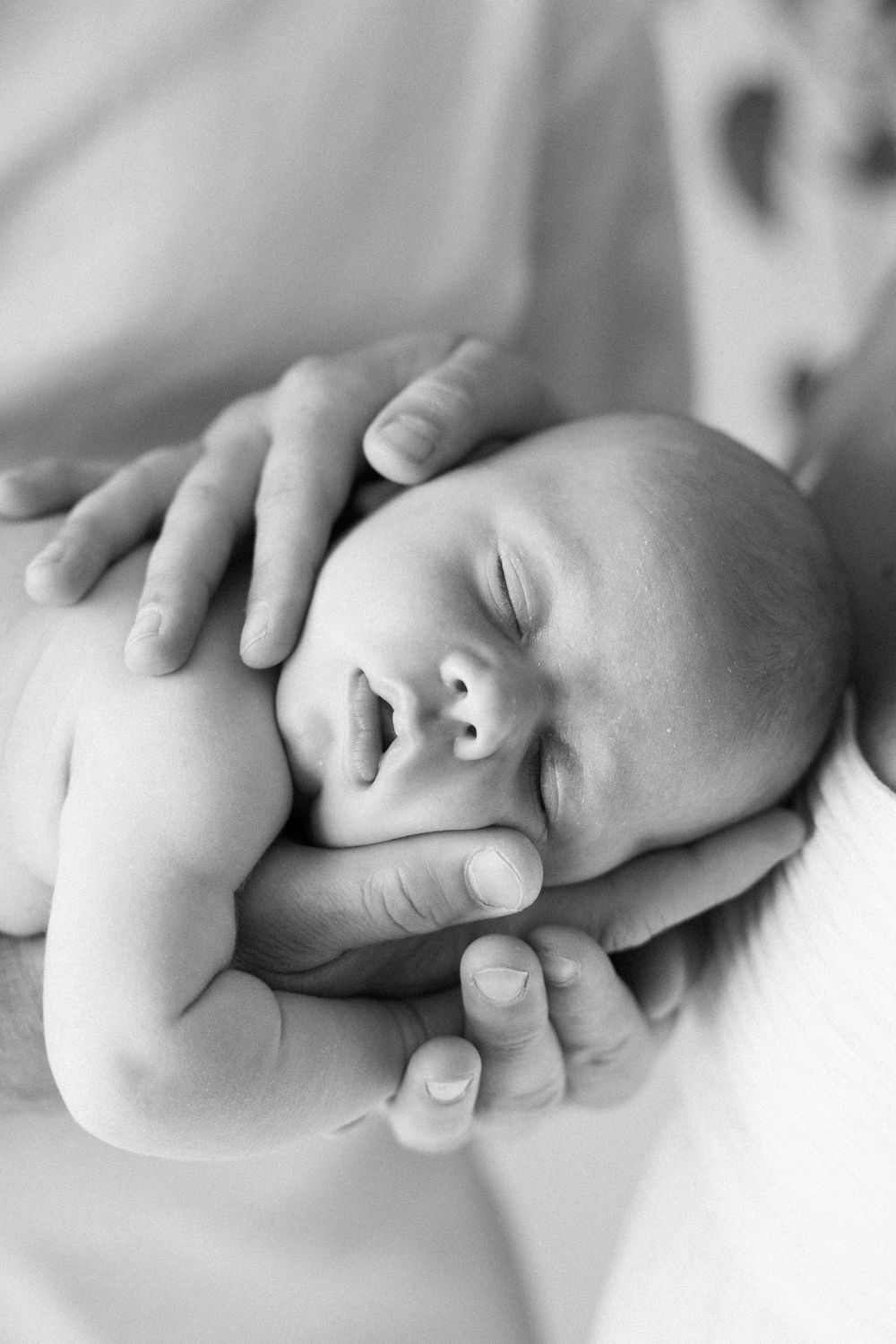 Black and white photo of a sleeping newborn baby cradled gently in adult hands.