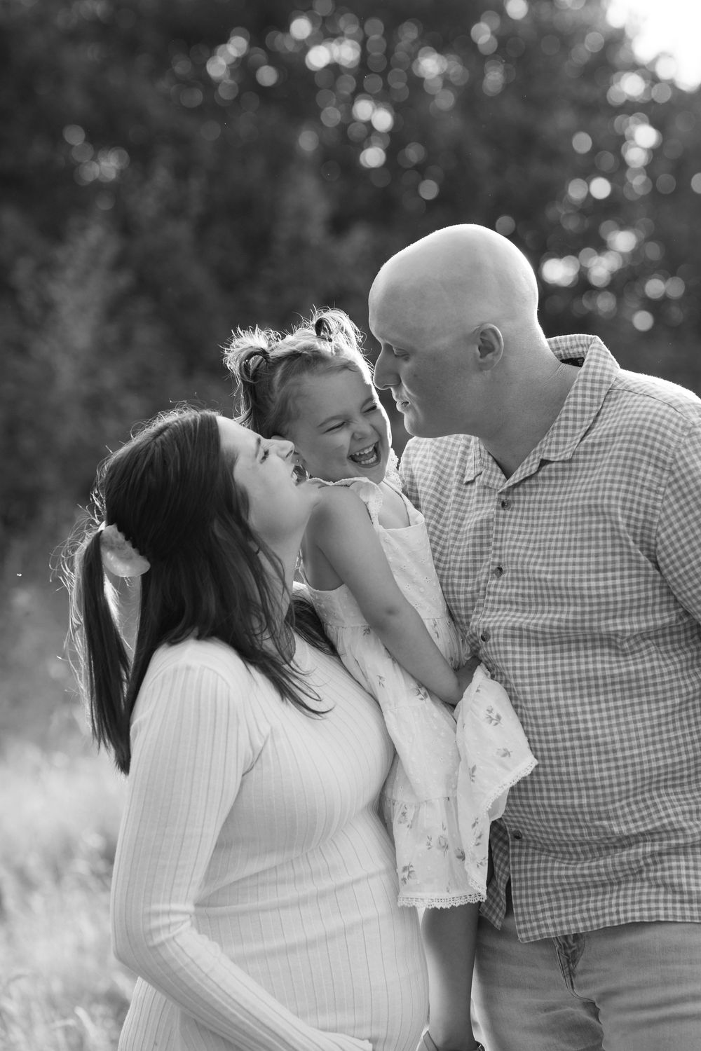 Black and white photo of pregnant mother and father laughing with their young daughter in an outdoor setting. Victoria, BC, Vancouver Island