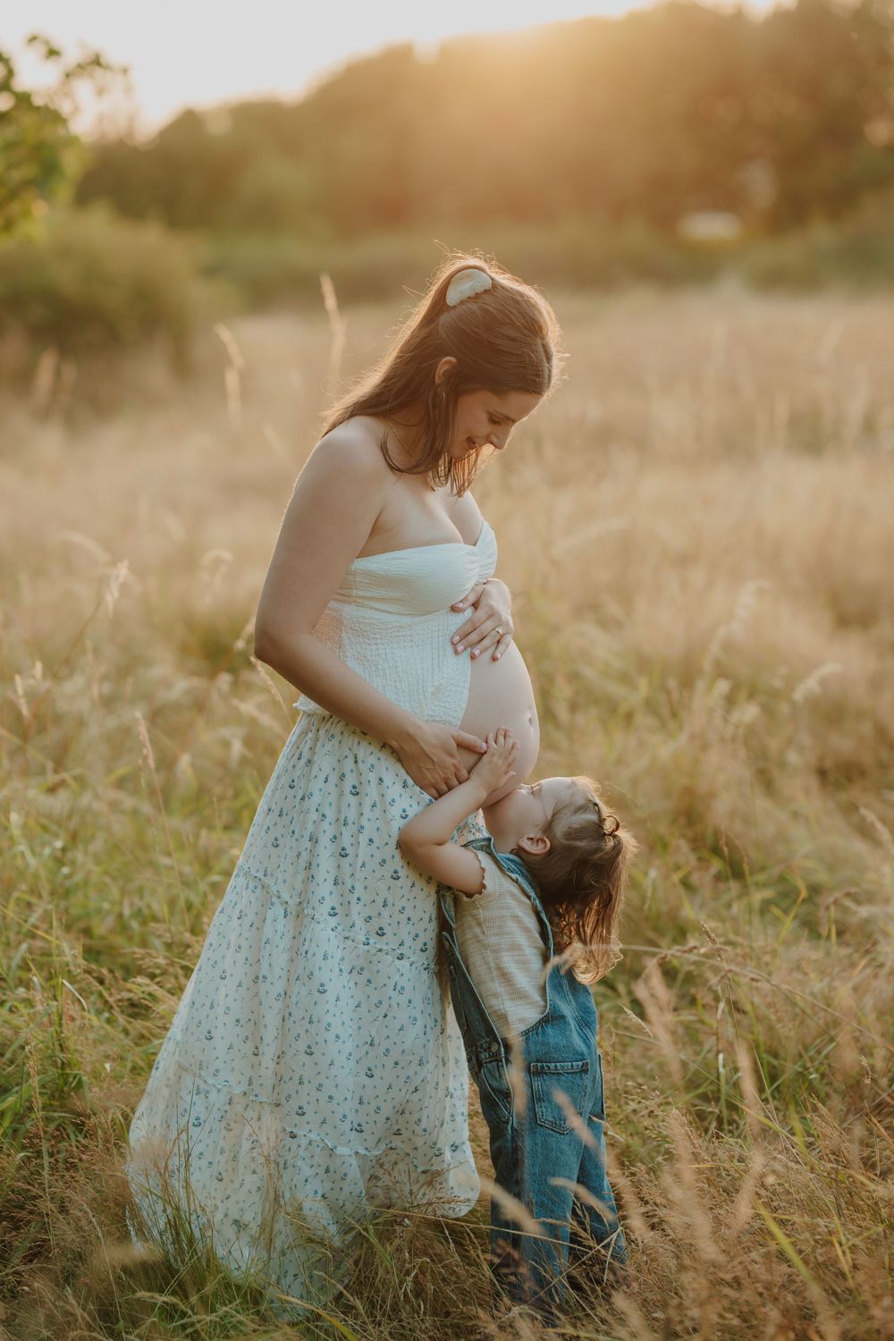 Pregnant woman in floral skirt sharing a tender sunset moment with her young daughter in a golden field. Victoria, BC, Vancouver Island.