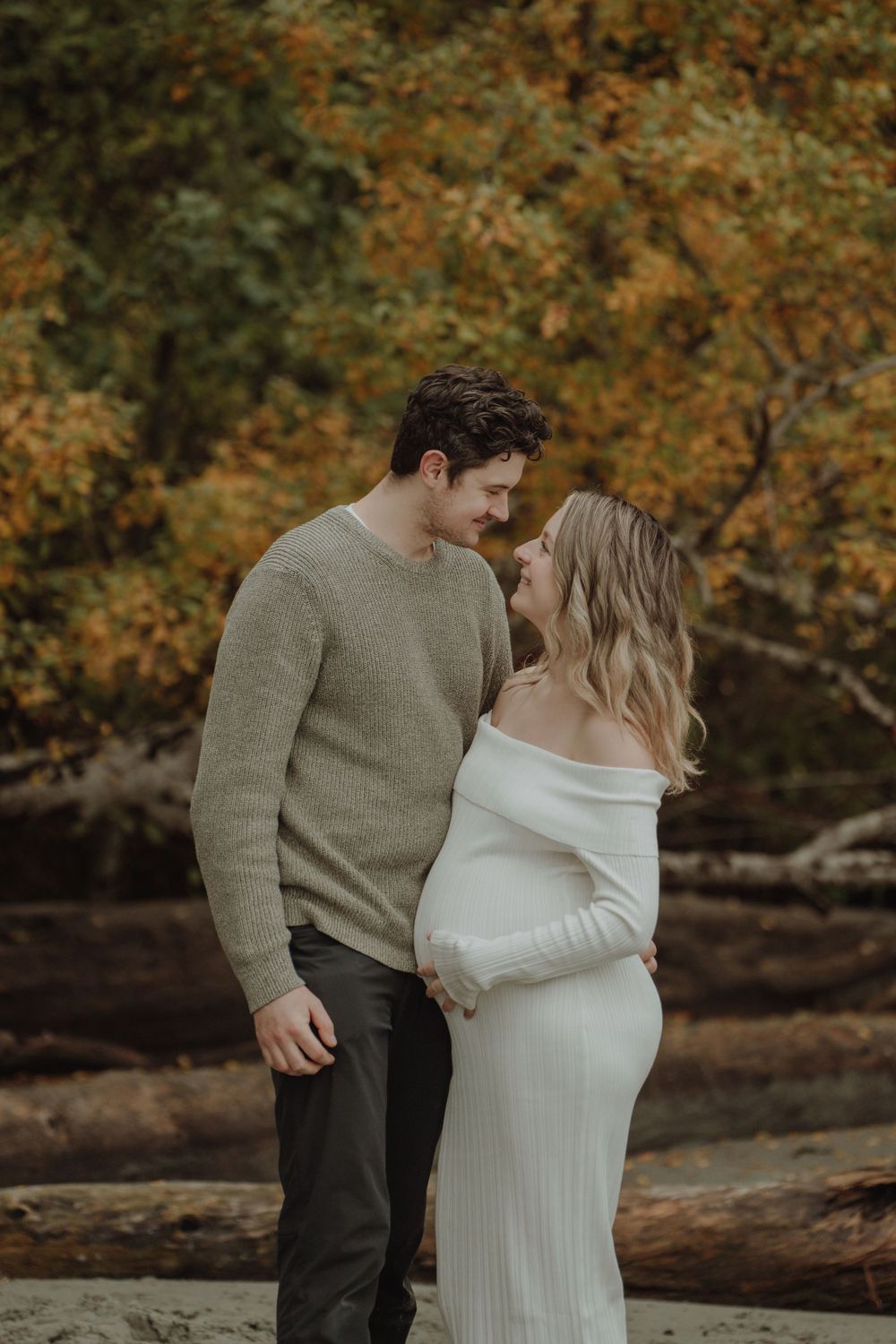 Expecting couple sharing tender forehead touch during fall maternity session on woodland beach.