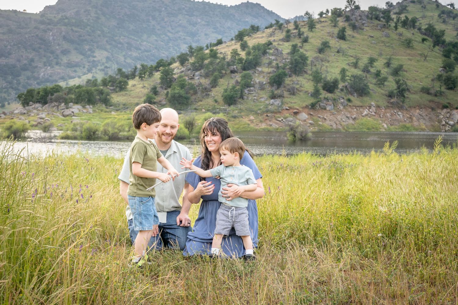 A group of people stand in a line together against a scenic mountain backdrop with green rolling hills and meadows.