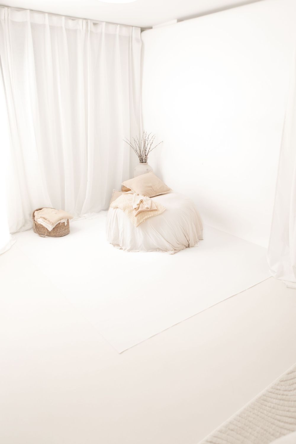 A minimalist all-white bedroom interior with soft curtains, bedding, and natural light creating a serene atmosphere.