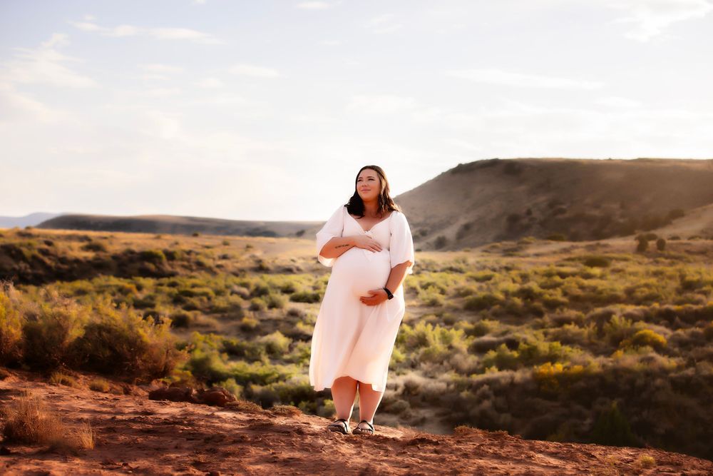 Person in a peach dress twirls joyfully at sunset in a desert landscape overlooking scenic red rock formations.