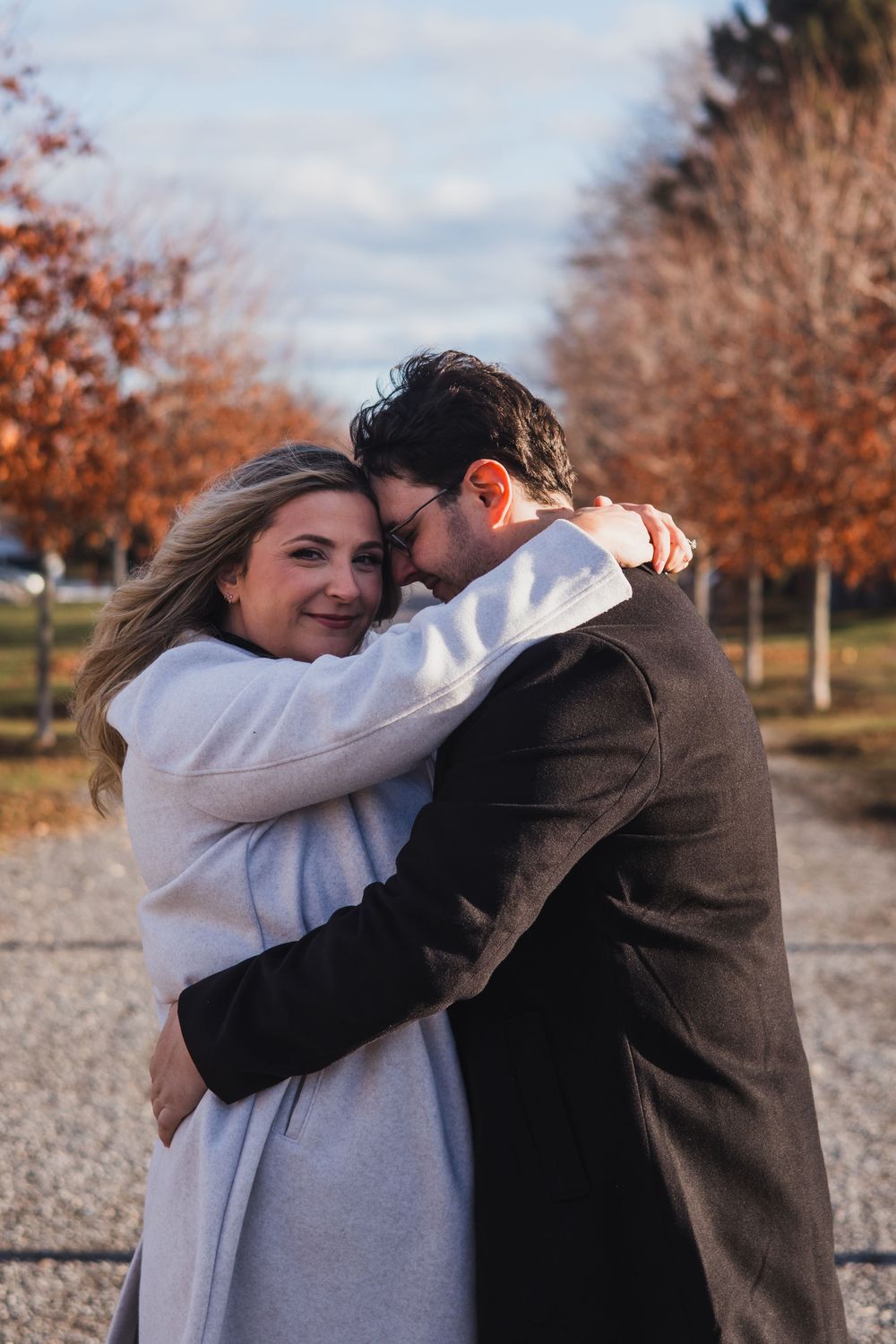 A couple embraces outdoors on an autumn day with orange trees in the background.