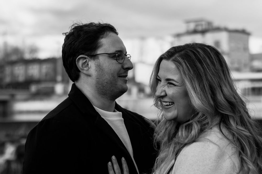 A romantic couple shares an intimate embrace against a blurred background during an outdoor photoshoot.