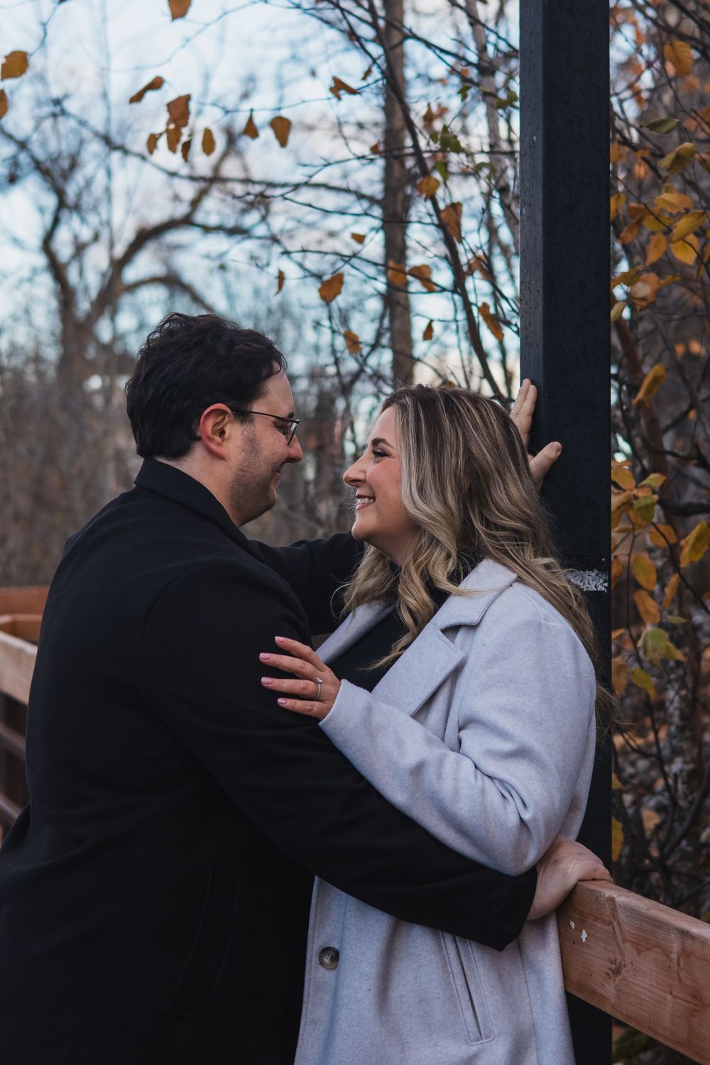 A couple laughs together on a wooden deck surrounded by autumn trees.