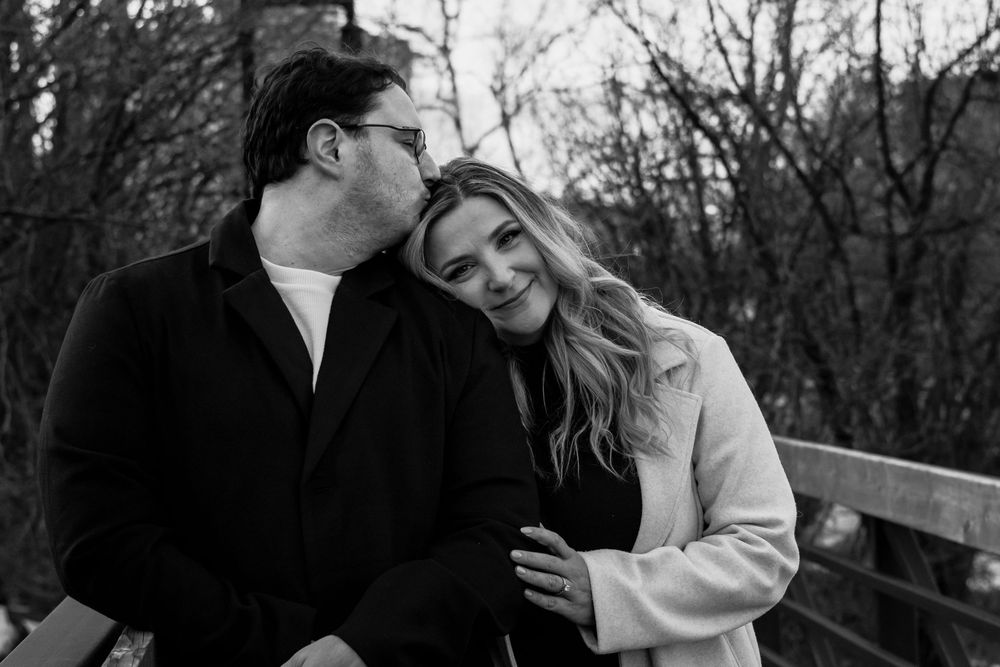 Black and white photo of a couple sharing a playful moment on a wooden deck.