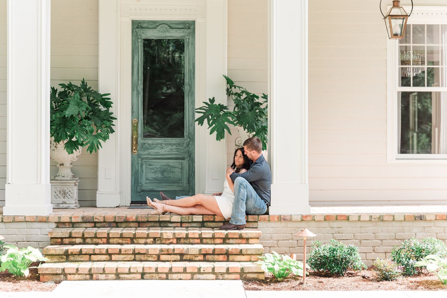 An engaged couple sitting on the front porch of a historic farmhouse at Whippoorwill Manor in Mayfield, KY.