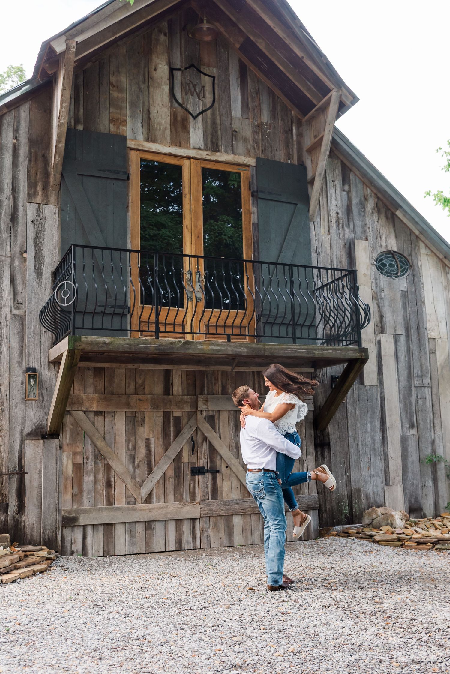 An engaged couple hugging and twirling in front of a barn at Whippoorwill Manor in Mayfield, KY.