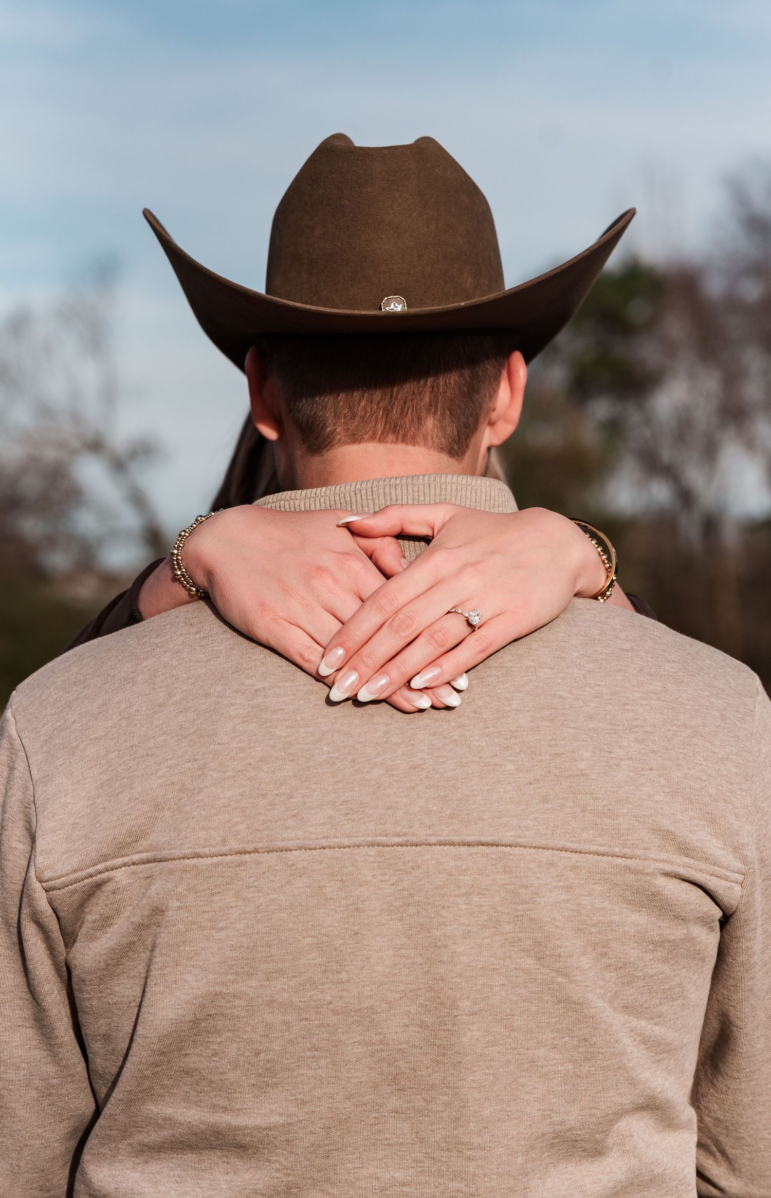 A fiancé with her hands wrapped around her cowboy showing off her engagement ring at a farm in Benton, KY.