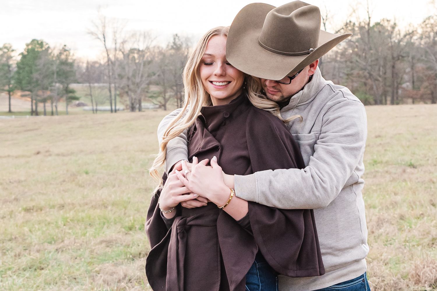 An engaged couple with cowboy hats on embracing each other in a field in Benton, KY.