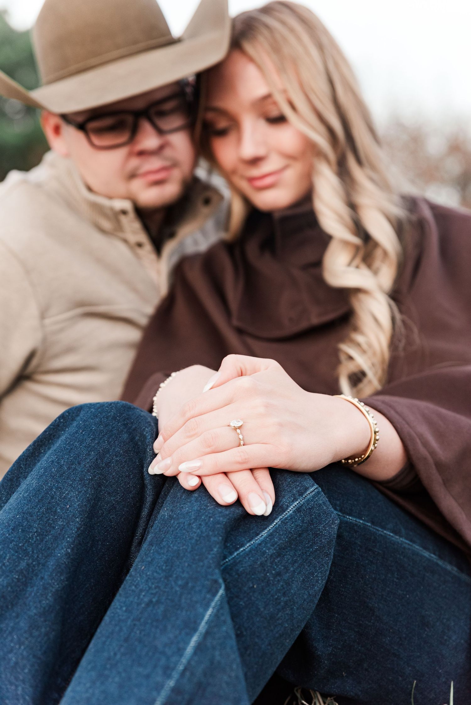 An engaged couple sitting down together with the engagement ring in focus on a farm in Benton, KY.