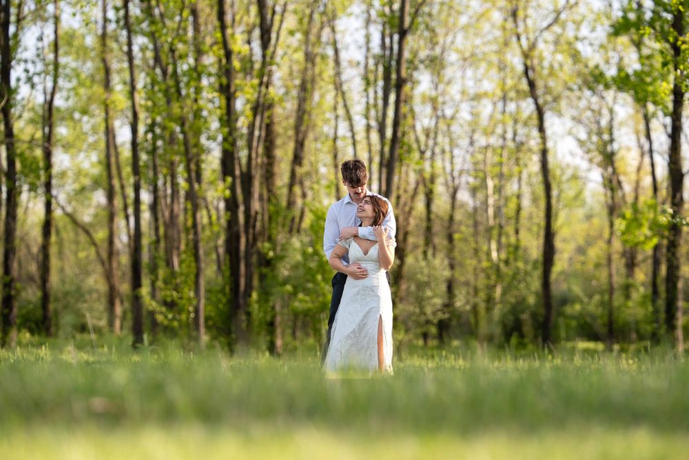 Couple embracing in a sunlit green meadow with lush trees in the background during an outdoor wedding.