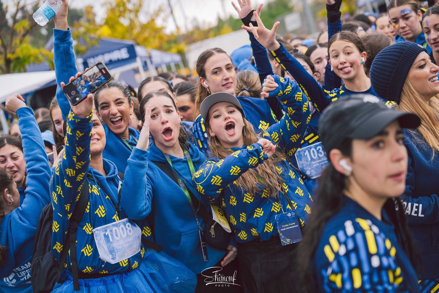 Group wearing matching blue jackets cheering enthusiastically outdoors during an event.