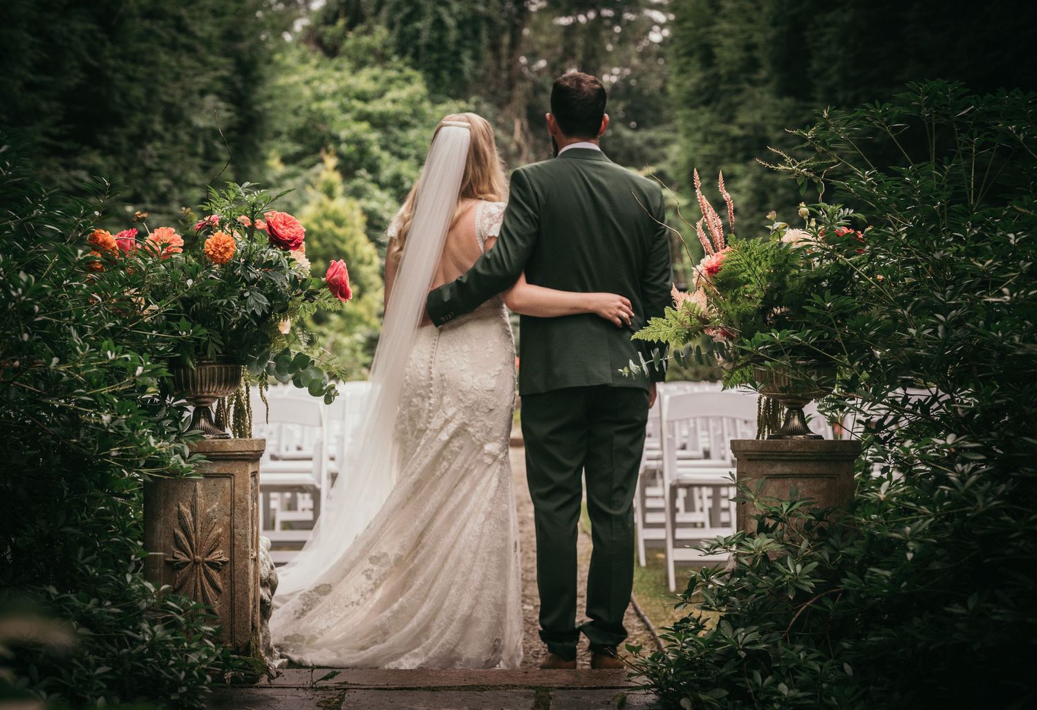 A bride and groom walk arm in arm through a lush garden wedding venue with colorful floral arrangements.