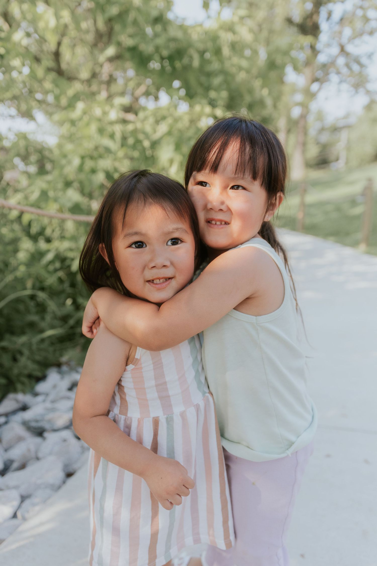 Two young children in summer dresses hugging and smiling outdoors.