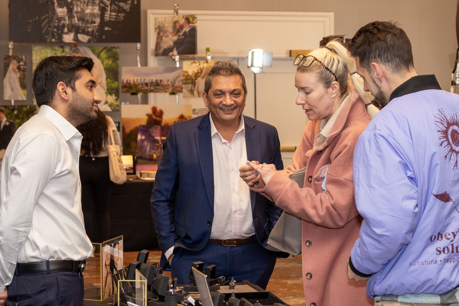 Group of people gathered around a display table at an indoor event examining items.
