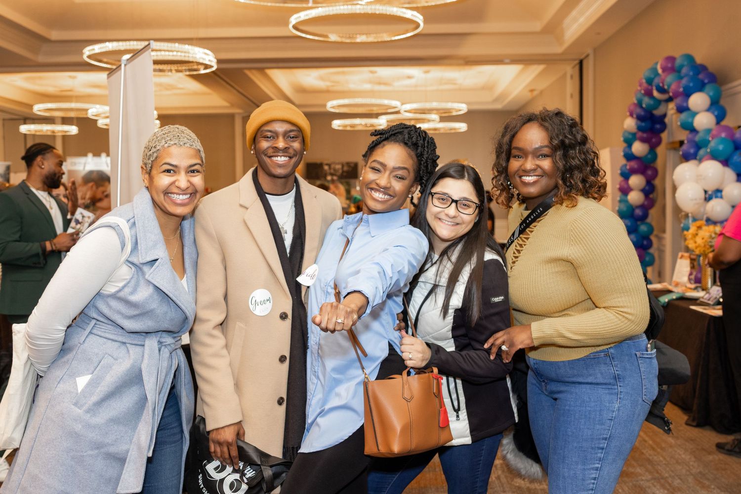 Diverse group of event attendees pose together in a ballroom with decorative lighting.