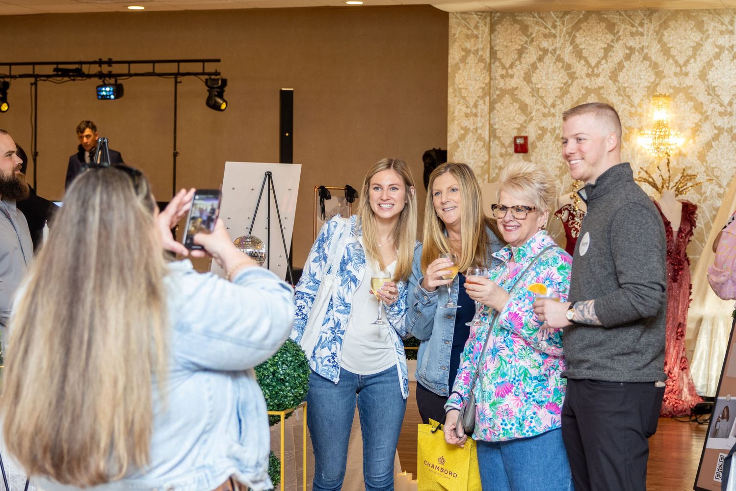 Group poses for a photo at an indoor event with decorative wallpaper background.