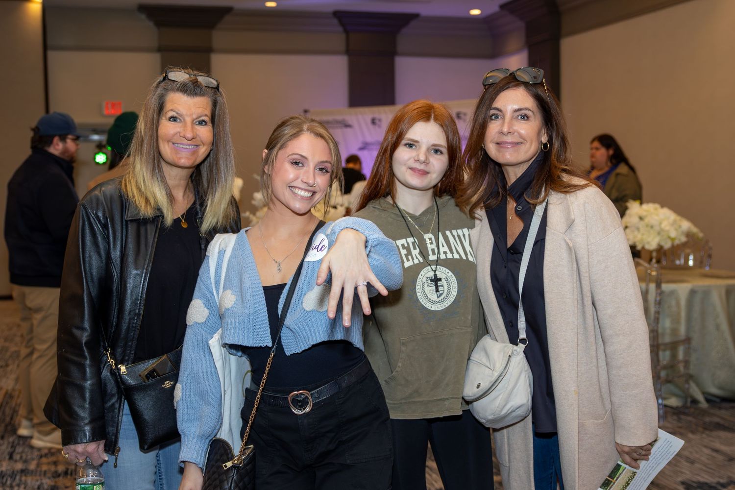 Group of friends showing off engagement ring at an indoor event.