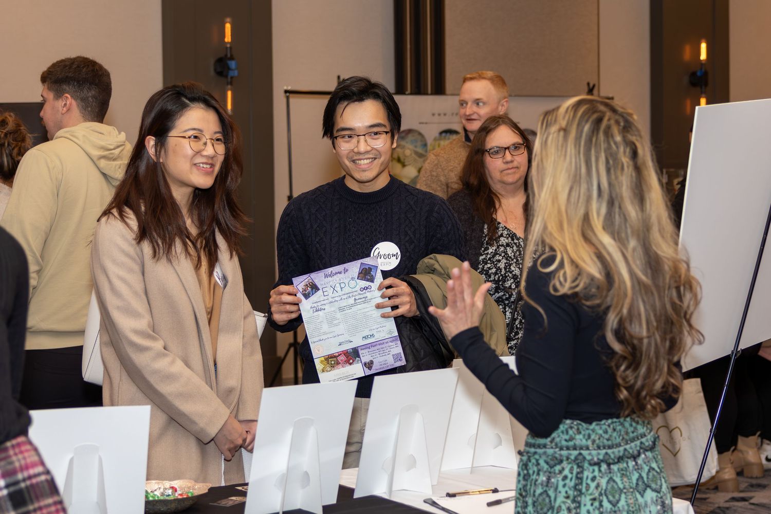 Event attendees reviewing paperwork at a vendor booth during an indoor exhibition.