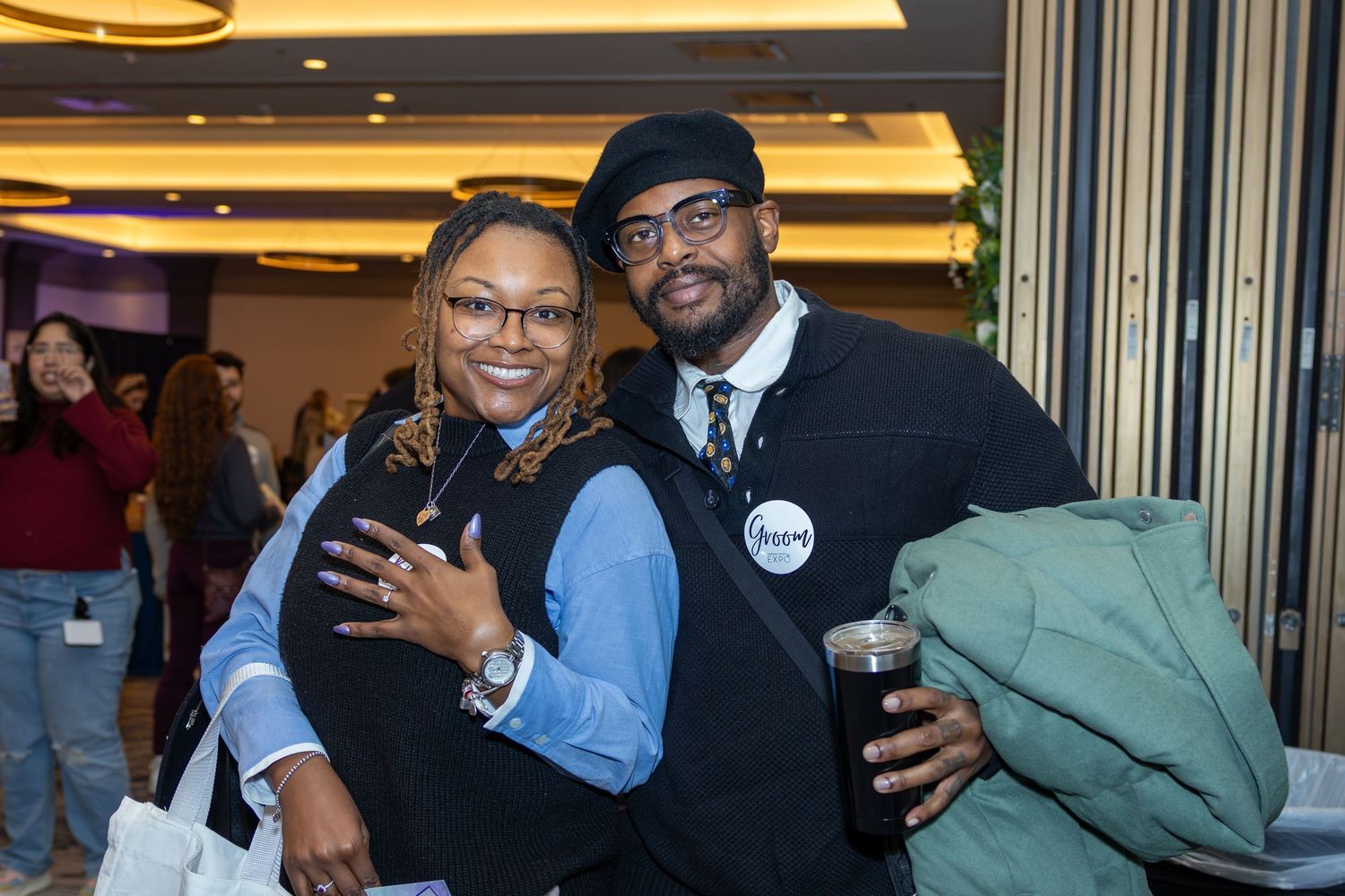 Two attendees share a happy moment at an indoor event with decorative lighting.