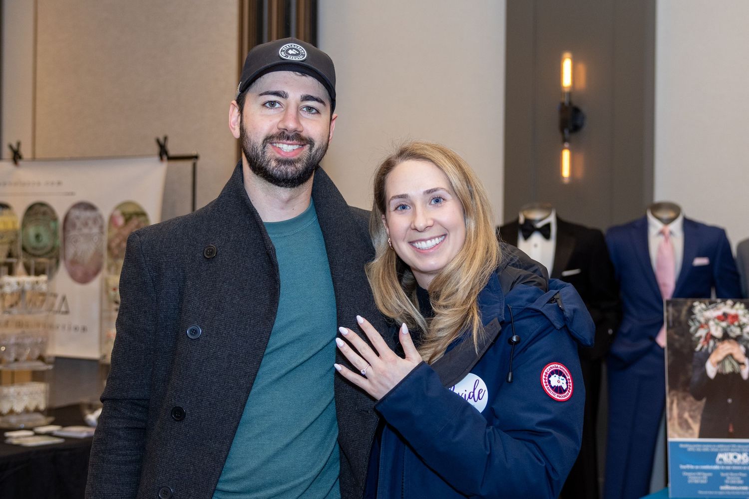 Couple poses at an event, with one wearing a Canada Goose jacket and the other in dark casual attire.