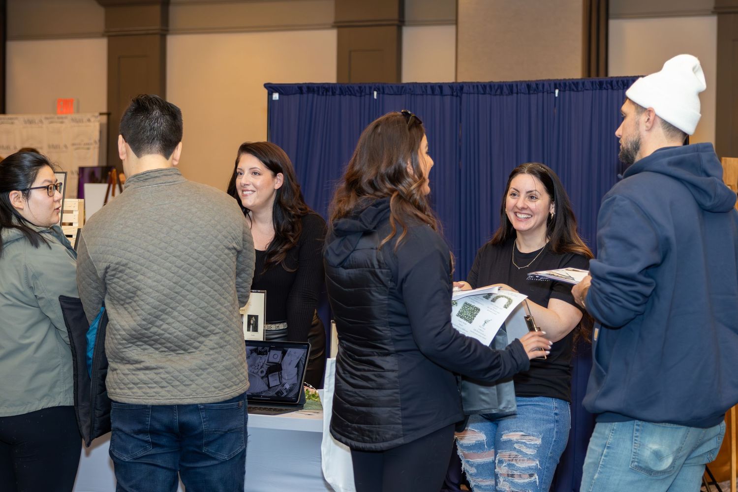 Group of attendees gather around a vendor booth at an indoor event.