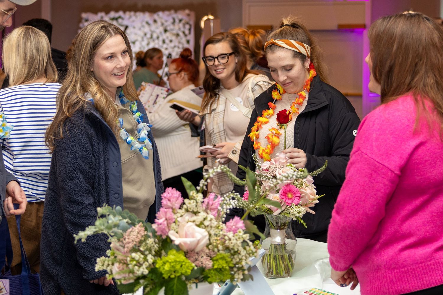 Guests gather around tables at a luxury event featuring elegant flower centerpieces and pink ambient lighting.