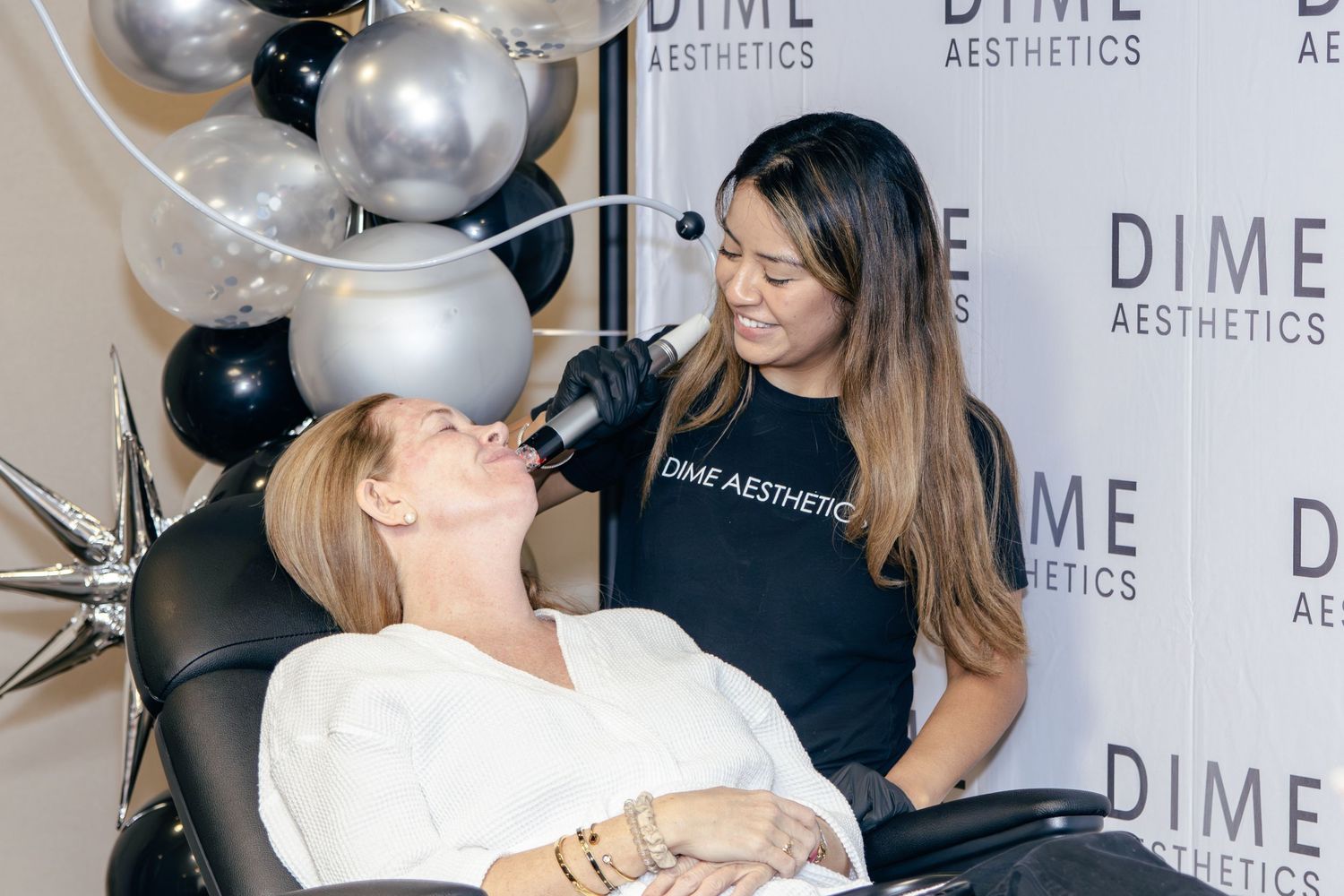 Celebratory moment captured at DIME Aesthetics event with silver and black balloon decorations.