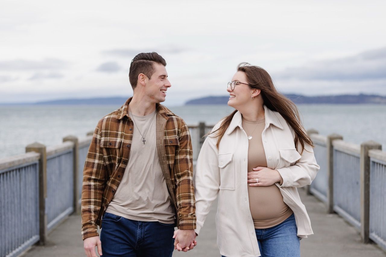 Expecting parents walking on a Mukilteo beach dock. Intimate and affectionate maternity photography by Tim Neal.