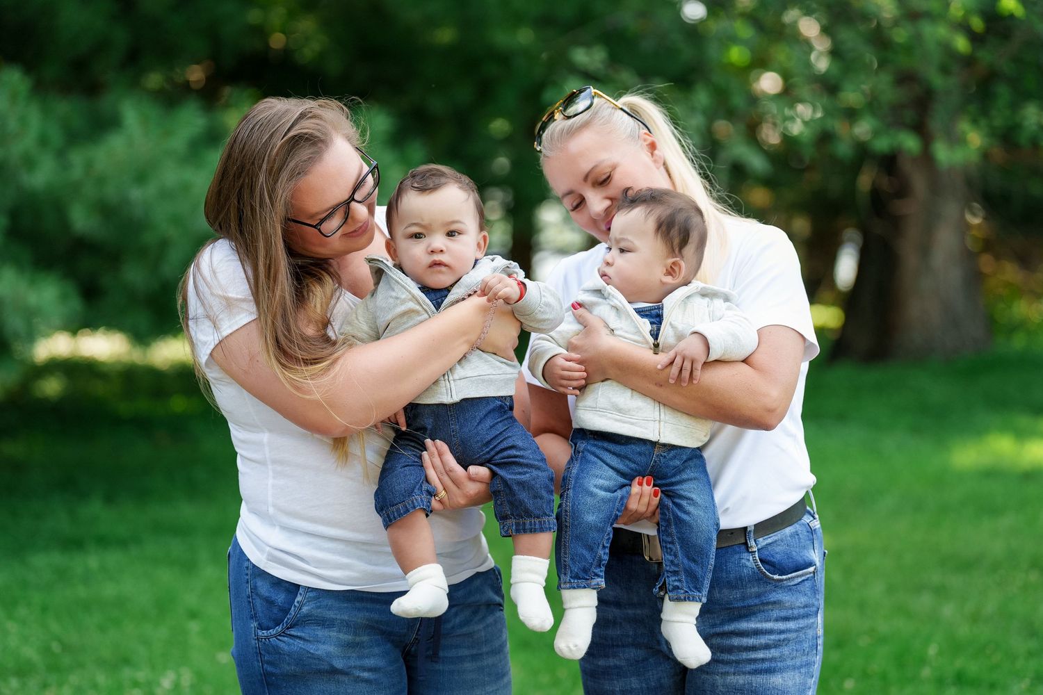 A family wearing coordinating white and denim outfits poses together in a sunny garden setting for outdoor portraits.
