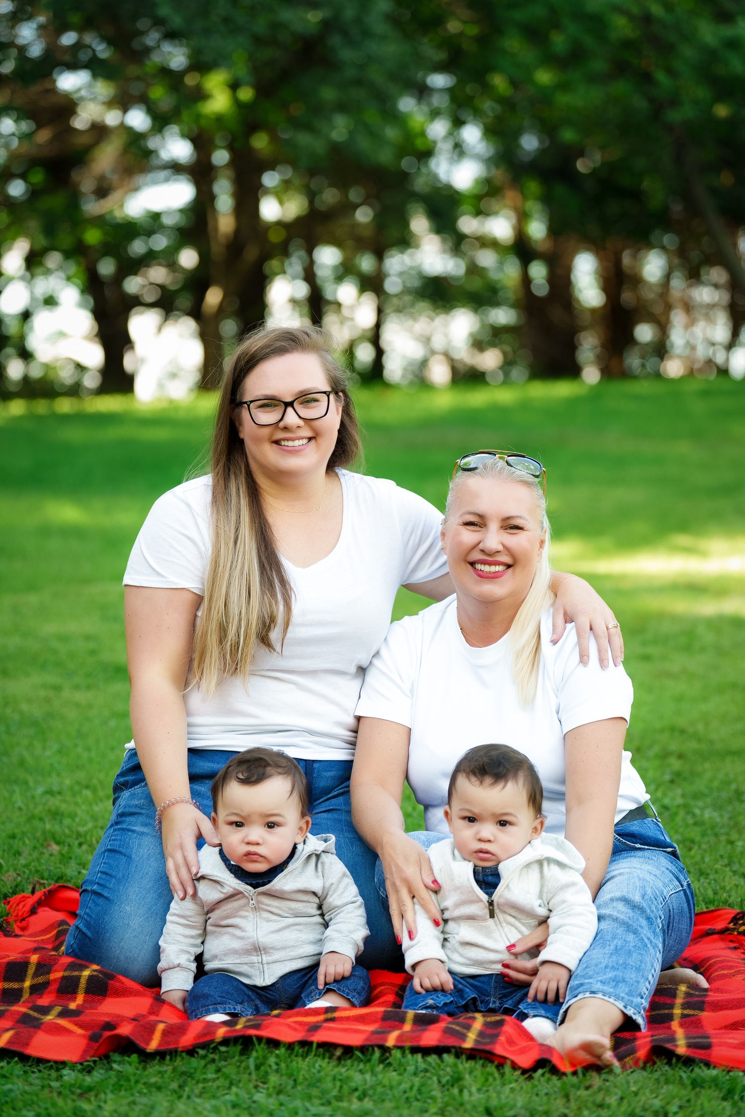 Family enjoying a sunny day together while sitting on a red blanket in a grassy park setting.