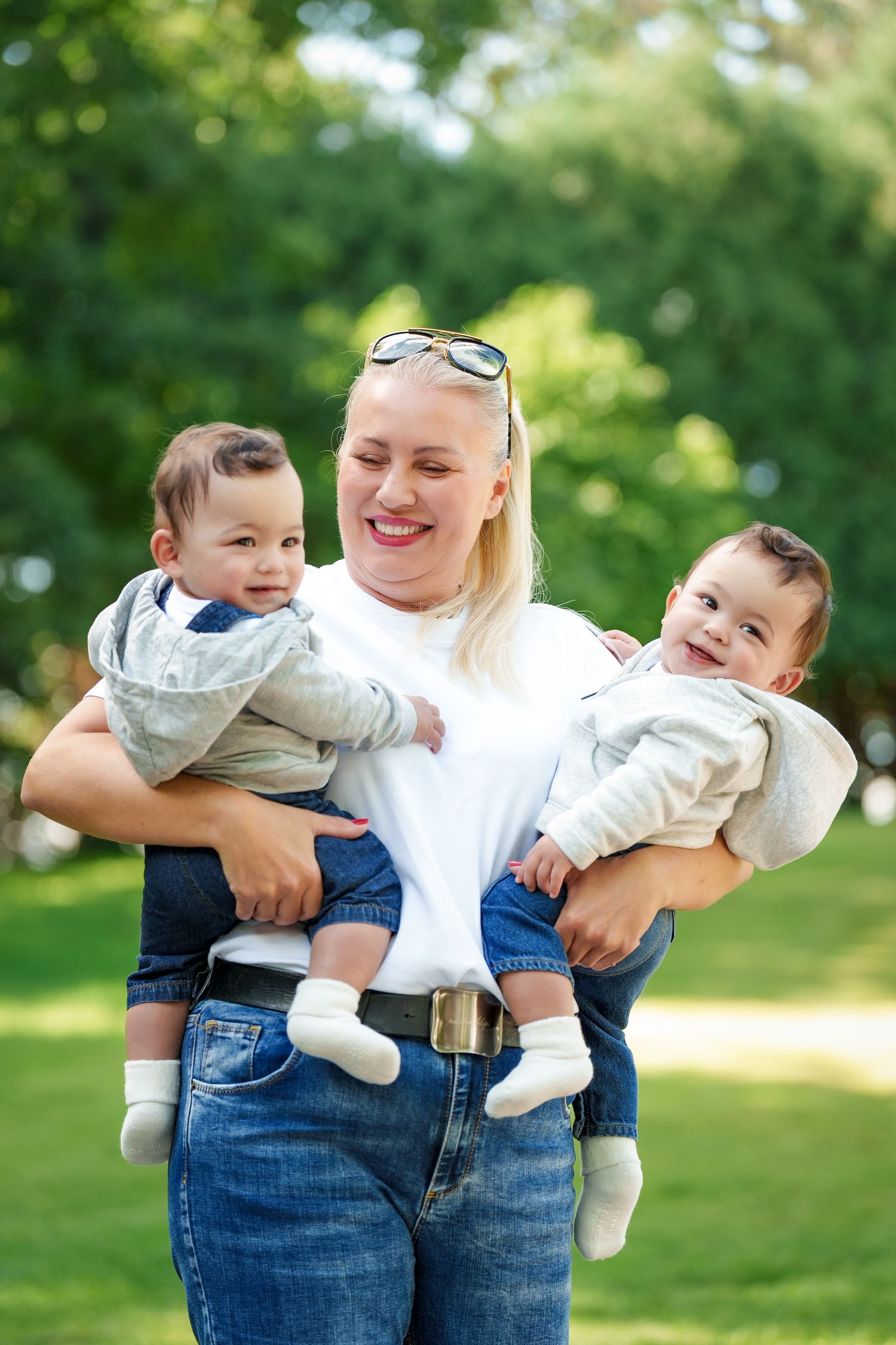 Parent and child share playful moments in a sunny park setting with green trees in background.