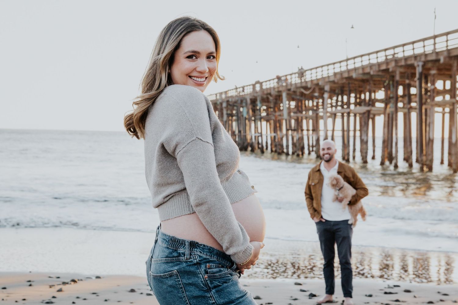 Maternity photo at a beach pier with subject turning to show baby bump in casual attire.