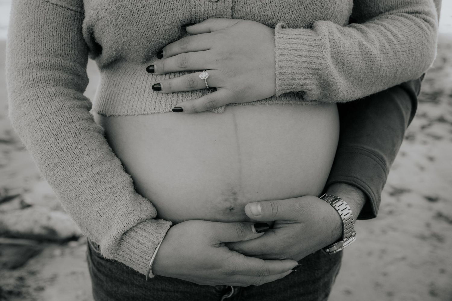 Black and white close-up of hands cradling a pregnant belly showing love and connection.