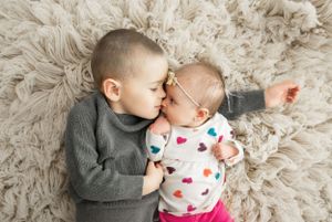 Two children sharing tender moment on plush carpet during photoshoot.