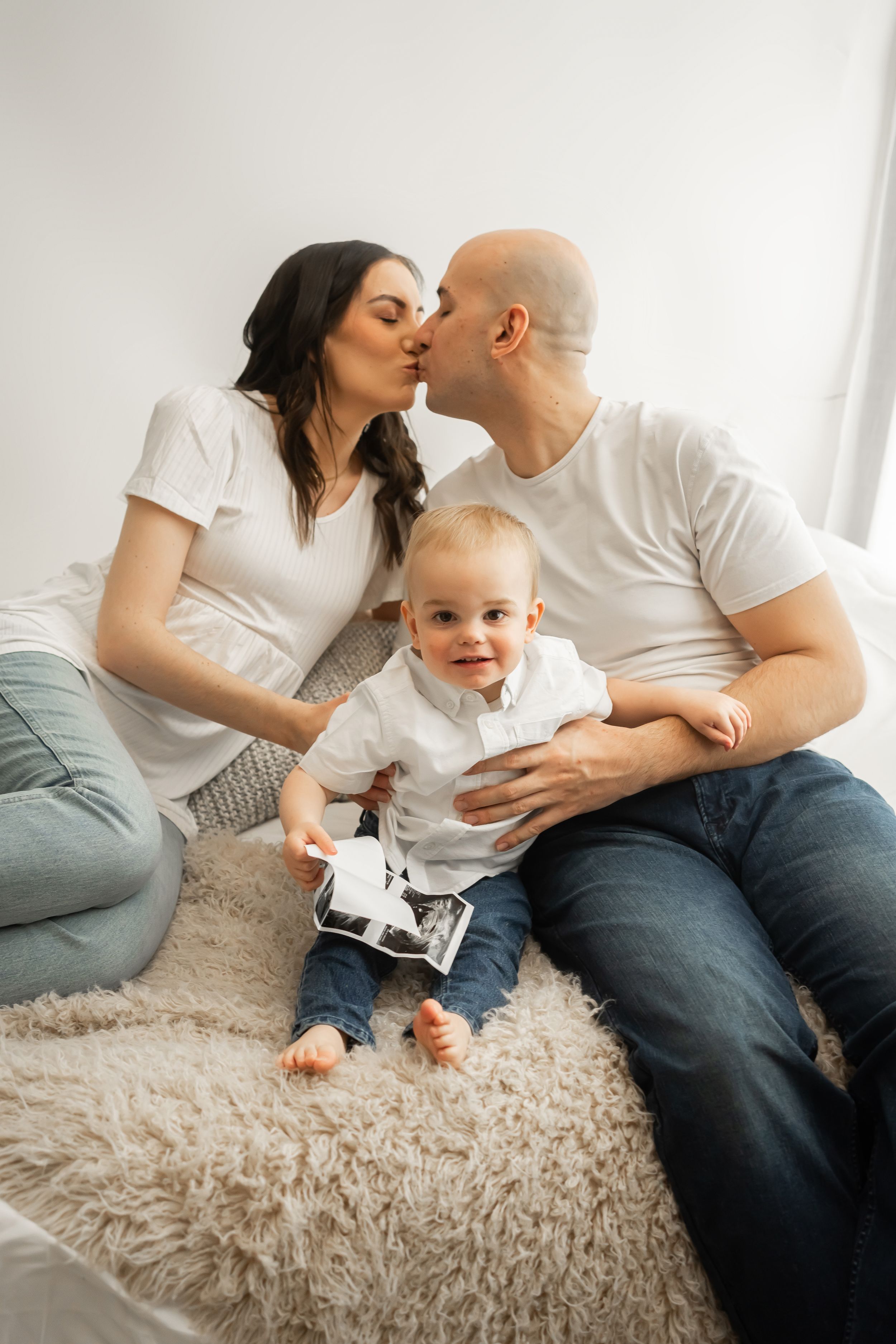 Parents sharing intimate moment while toddler plays with ultrasound photos.