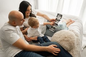 Parents showing ultrasound images to excited toddler on bed.