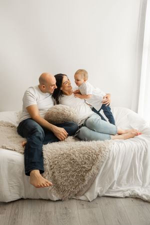 Candid family moment captured on white bed with plush throw blanket.