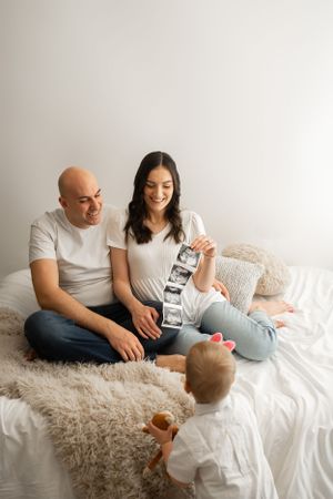 Parents showing ultrasound strip to child during intimate family photoshoot.