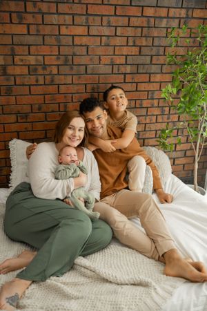 Cozy family moment on white bedding with brick wall backdrop and indoor plant.