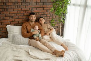 Family cuddle session photographed against warm brick wall with natural window lighting.