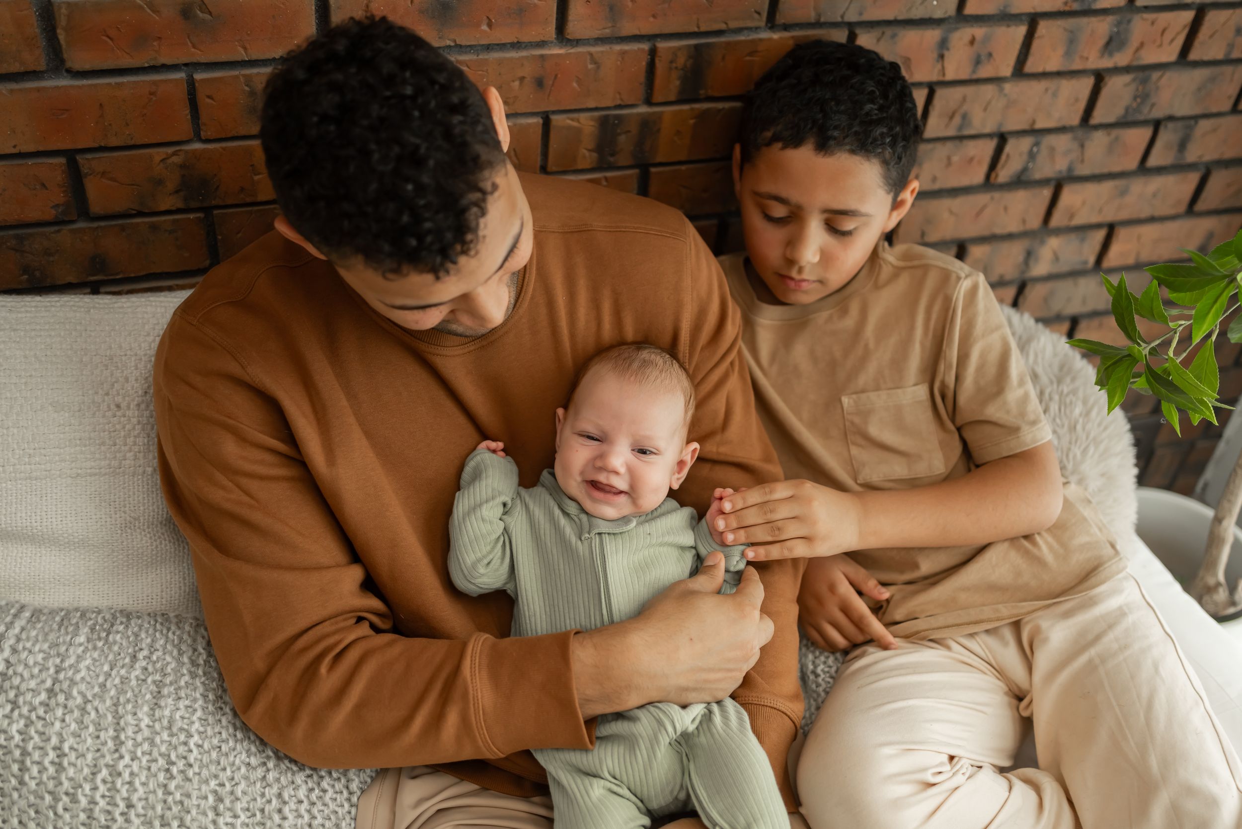 Loving family moment captured in natural light with brick wall background.