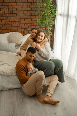 Family lifestyle portrait on gray flooring with exposed brick wall and white curtains.