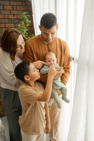 Family playing together with a baby in a warm embrace, wearing matching beige outfits in a bright home setting.