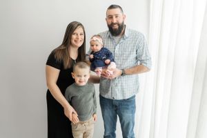 Studio family portrait with parents and two children against white wall.