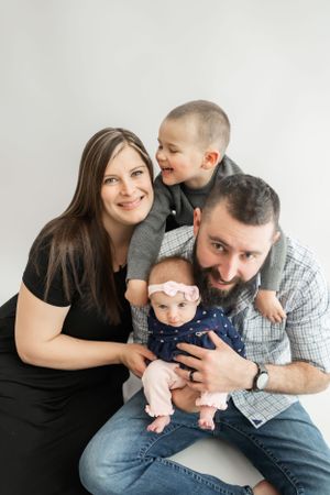 Casual family photo with parents and two children against white background.